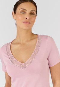 Top rosa a maniche corte con scollo a V e dettagli in pizzo, dal design aderente, realizzato in tessuto morbido e liscio.