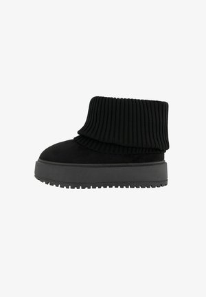 Schwarze Knöchelstiefel mit einem gerippten Strickkragen und einer flachen, strukturierten Sohle. Hergestellt aus einer Kombination aus Wildleder und elastischen Materialien.