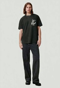 Black cotton T-shirt with a front graphic design, paired with loose-fitting black denim jeans and black shoes. Simple design and relaxed fit.