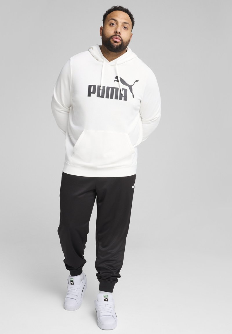 Hanorac alb cu glugă, având logo-ul „PUMA” în negru, asortat cu pantaloni jogger negri și adidași albi. Material moale, croi casual, design simplu.