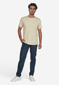 Gestreiftes beige T-Shirt mit kurzen Ärmeln und Rundhalsausschnitt, kombiniert mit dunkelblauen Hosen und weißen Sneakers. Lässiges Outfit mit bequemer Passform.