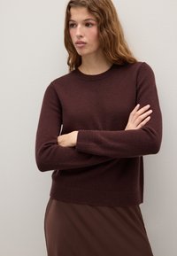 Burgunderfarbener Strickpullover mit langen Ärmeln, Rundhalsausschnitt, gerippten Bündchen und Saum. Glatte Textur und lockere Passform in Kombination mit einem braunen Rock.