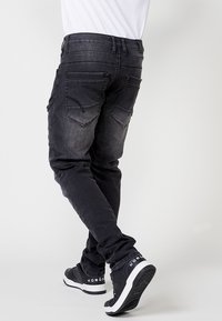 Črne jeans hlače s številnimi žepi, slim fit, zbledela tekstura in kontrastno šivanje; v kompletu s črnimi supergami z belimi akcenti.