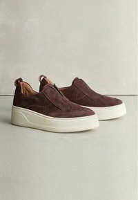 Braune Wildleder Slipper verfügen über eine gepolsterte weiße Sohle, eine glatte Textur und sichtbare Nähte. Mit einem praktischen Zuglasche für einfaches Anziehen.