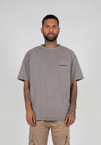Gray oversized t-shirt in a faded wash, featuring a round neck and short sleeves. Small black logo accent on the left chest area.