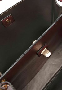 Interieur van een bruine leren handtas, met een gladde textuur, metalen sluiting en een subtiele stiknaad langs de randen.