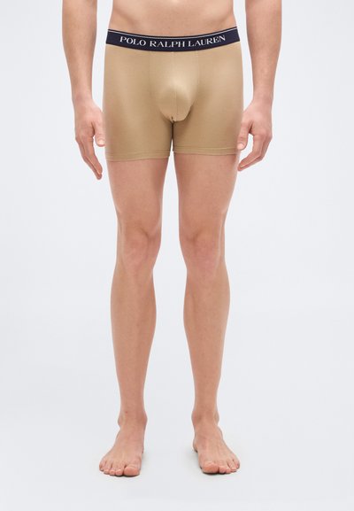 Μπεζ μποξεράκια με ναυτικό μπλε ζωνάκι μέσης, με την ετικέτα "POLO RALPH LAUREN." Διαθέτουν εφαρμοστή σχεδίαση και απαλό ύφασμα, φτάνοντας ως το μέσο του μηρού.