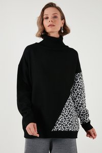 Donna che indossa un maglione nero a collo alto con un motivo leopardato bianco e nero che copre una manica e parte della parte anteriore.