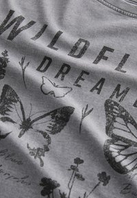 T-shirt en coton gris avec texte imprimé noir « WILDFLOWER DREAMS » et illustrations de papillons et de fleurs à l'aspect texturé.