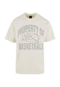 Kremfarget bomulls T-skjorte med et stort grått trykk som leser "PROPERTY OF k1x BASKETBALL" i fet, sporty skrifttype. Korte ermer, rund hals.