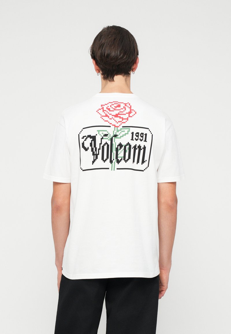 T-shirt en coton blanc avec un graphique de rose pixelisé, le texte "Volcom" et "1991" en noir, manches courtes et col rond.