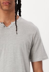 Grå og hvid stribet T-shirt med Henley-udskæring, der har to knapper og korte ærmer. Fremstillet af blødt, tekstureret stof.
