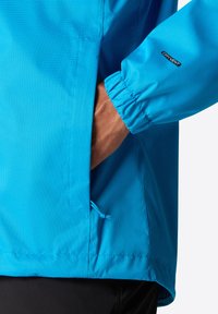 Lehká modrá bunda s texturovaným povrchem, elastickými manžetami a boční kapsou se stahovací šňůrkou. Obsahuje štítek "DRYVENT".