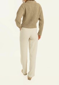 Beige gestrickter Pullover mit strukturiertem Design und geripptem Saum, kombiniert mit hochtaillierten, hellen Hosen, die seitliche Taschen haben.