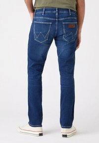 Jeans de denim azul con un ajuste slim, con costuras en contraste, dos bolsillos traseros con distintivas adornos y una etiqueta de cuero en la cinturilla.