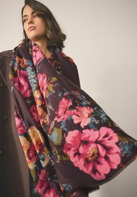 Blomstret sjal i mørke nuancer, med store lyserøde og blå blomster. Blød tekstur med frynsekanter, elegant draperet over en model.