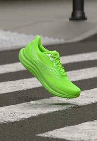 Φωτεινό πράσινο παπούτσι για τρέξιμο που αιωρείται πάνω από διάβαση πεζών σε ασφαλτοστρωμένο δρόμο.