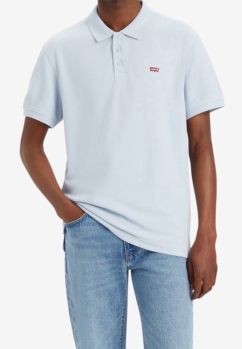 Ljusblå pikétröja i mjuk bomull med krage, tre knappar och en liten röd Levi's-logga på bröstet. Bärs med denimjeans.