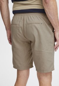 Beige rövidnadrág, rugalmas derékkal, két hátsó zsebbel rejtett díszítéssel és könnyű, texturált anyagú kivitelezéssel.