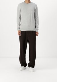 Maglione grigio dalla texture con maniche lunghe, abbinato a pantaloni marroni larghi e sneakers bianche. Collo rotondo semplice e polsini a costine.
