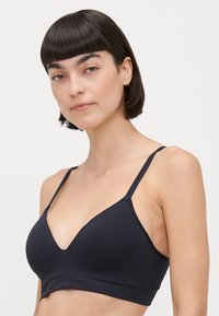 Melnā trīsstūrveida krūšturis ar plānām regulējamām siksnām, bezšuvju dizains un V formas kakla izgriezums. Mīksta, elastīga auduma ar gludu tekstūru.