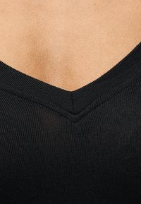 Κοντινό πλάνο ενός μαύρου ριγωτού ρούχου με V-λαιμόκοψη σε ανοιχτόχρωμο δέρμα.