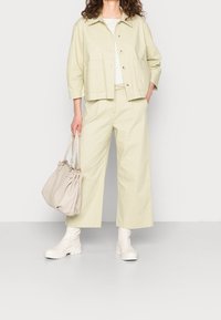 Ljusgrön kort jacka med två framfickor, matchande vida byxor, vit rutig topp, beige handväska och vita klumpiga stövlar.