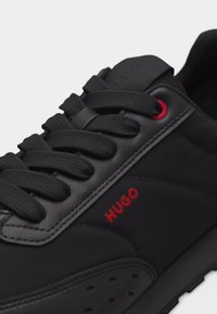 Melns sporta apavu ar biezām šņorēm, sarkanu aci, sarkanu "HUGO" logotipu sānos, polsterētu apkakli un detalizētu šuvumu uz sintētiskā augšdaļas.