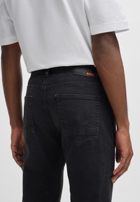 Slim-fit černé džíny vyrobené z denimu, s jemným vyblednutím, zadními kapsami a značkovým černým koženým páskem s oranžovým logem.