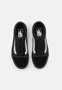 Un paio di sneakers Vans Old Skool nere con strisce bianche ai lati e lacci neri su uno sfondo bianco semplice.