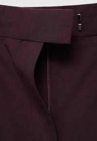 Dark purple fabric with a smooth texture featuring a waistband, zipper, and metallic accents. Clean lines and tailored design details.