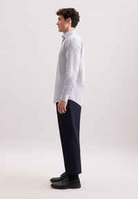 Camicia button-up a righe blu chiaro con maniche lunghe, abbinata a pantaloni tailored blu navy e scarpe nere stringate. Vista laterale.