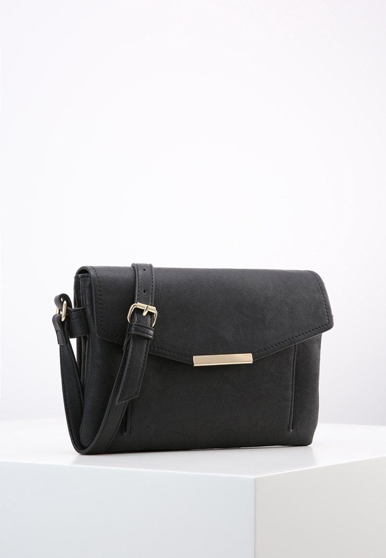 Borsa a tracolla nera in pelle con tracolla regolabile e chiusura rettangolare dorata su un piedistallo bianco.