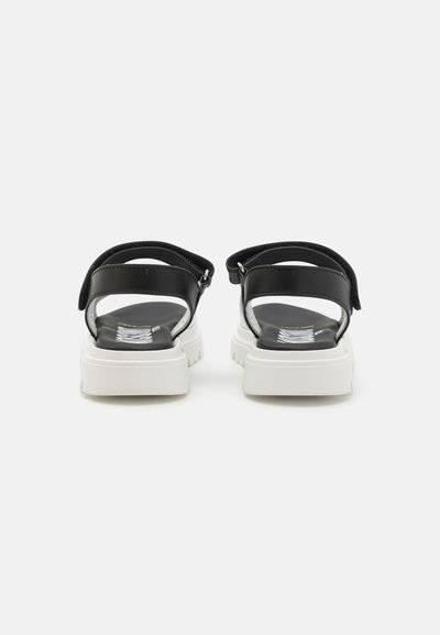 Sandalias negras con correas ajustables, suelas gruesas blancas, material suave y plantilla texturizada. Vista trasera que muestra el diseño de las correas y los detalles de la suela.