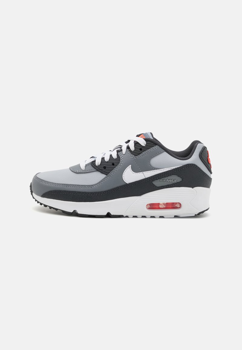 Γκρι και μαύρα αθλητικά παπούτσια Nike Air Max 90 με λευκές λεπτομέρειες, διαθέτοντας υφή στο επάνω μέρος, επιpronounced αερόσυστημα και κόκκινη λεπτομέρεια στη φτέρνα.