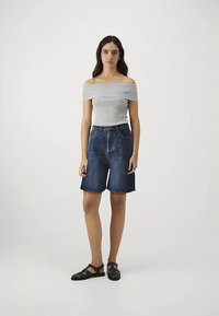 Pečių neuždengiantis pilkas megztinis su trumpomis rankovėmis, derinamas su mėlynais džinsiniais šortais iki kelių. Juodos basutės užbaigia įvaizdį.