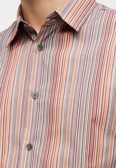 Ε γγύς πλάνο κορμού που φοράει πουκάμισο με πολύχρωμες κάθετες ρίγες, γκρι κουμπιά και μυτερό γιακά.
