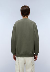 Olijfgroene sweatshirt met lange mouwen, ronde hals en geribde manchetten. Gecombineerd met lichtgekleurde cargobroek met meerdere zakken.