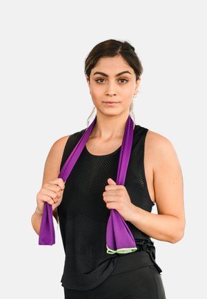 Schwarzes ärmelloses Oberteil und schwarze Trainingshose; sie hält zwei lila Widerstandsbänder, die eine strukturierte Oberfläche und grüne Akzente haben.