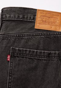 Poche arrière d’un jean Levi's noir avec étiquette rouge visible Levi's et écusson en cuir beige sur la ceinture.