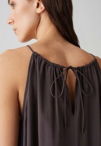 Dunkelgrau ärmelloses Top mit gerafftem Ausschnitt und gebundenem Verschluss auf der Rückseite, gefertigt aus leichtem Stoff mit glatter Textur.