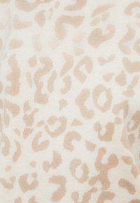 Ύφασμα με μοτίβο λεοπάρ σε ανοιχτό μπεζ και εκρού, με ποικίλα υφασμένα σημεία, δημιουργώντας ένα απαλό, ηπιωμένο πρότυπο σε πλεκτή επιφάνεια.