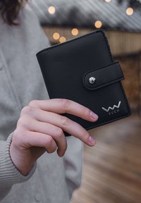 Black leather wallet with a silver snap button and embossed logo. Compact design, featuring smooth texture and clean lines, held in a hand.
