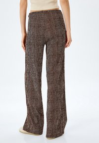 Bruine wijd-uitlopende broek met verticale witte strepen, gemaakt van textuurstof. Elastische tailleband, zachte afwerking, slepend zoom.
