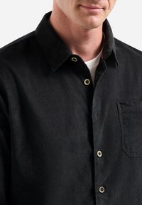 Zwarte corduroy overhemd met een button-down kraag, voorzien van een borstzak en contrasterende knopen voor extra detail. Gladde textuur.