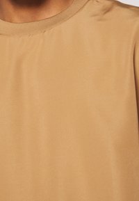 Camisa corta de manga corta color beige, con cuello redondo, hecha de tela suave. Presenta un diseño sencillo y una textura suave, sin patrones visibles.