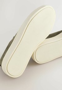 Grå ruskindssko med hvide gummisåler, der har en tekstureret overflade og afrundede kanter. Sålerne har et mønstret greb for bedre traction.