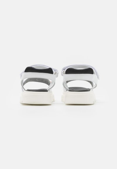 Sandales blanches avec un design de bride noir et blanc. Elles présentent une semelle épaisse et un dos ouvert, affichant un look minimaliste et moderne.