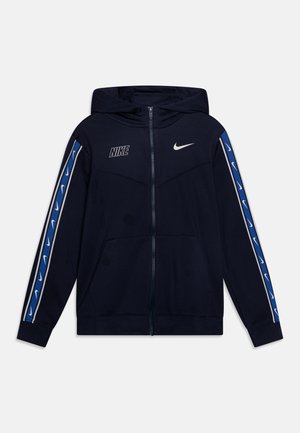 Sudadera con cremallera de Nike en azul marino, con capucha, bolsillos frontales, el swoosh y el logo de Nike en blanco en el pecho, y rayas azules con swooshes blancos en las mangas.