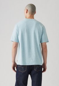 Lyseblå t-shirt med korte ærmer lavet af tekstureret stof. Har en klassisk rund halsudskæring og et lille logo-tag nær sømmen. Bæres med mørke denimjeans.